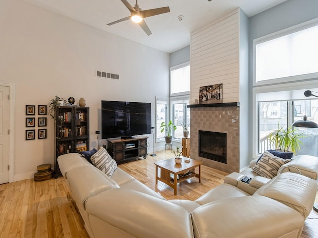 living room with ceiling fan, a towering ceiling, a fireplace, and light wood-type flooring