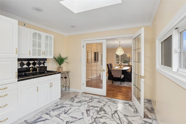 kitchen featuring white cabinetry, sink, hanging light fixtures, ornamental molding, and french doors