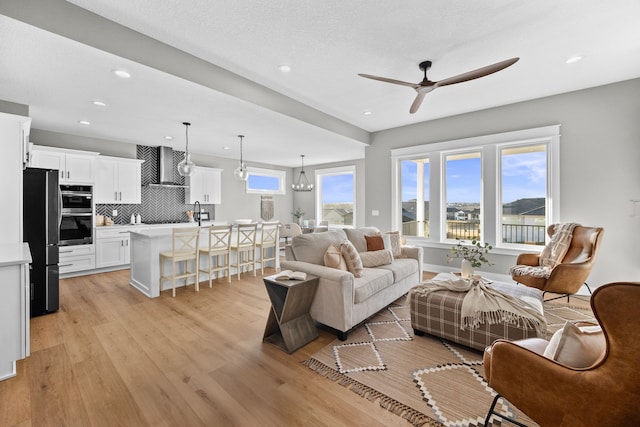 living area featuring ceiling fan with notable chandelier, light wood finished floors, baseboards, and recessed lighting