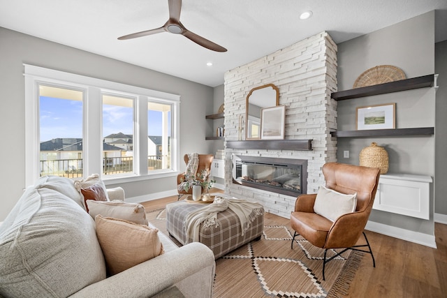 living area with a stone fireplace, wood finished floors, a ceiling fan, and baseboards