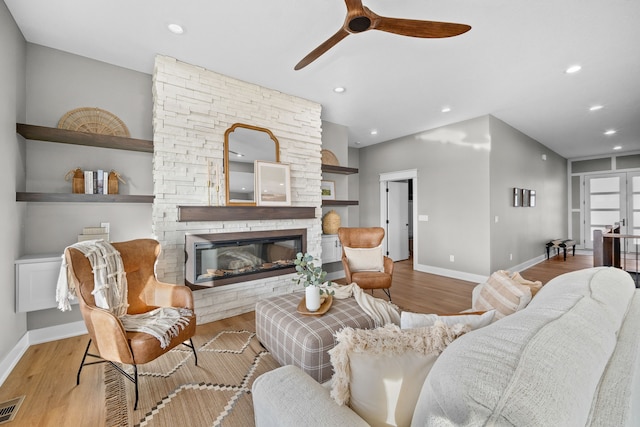 living area with a stone fireplace, wood finished floors, visible vents, and baseboards