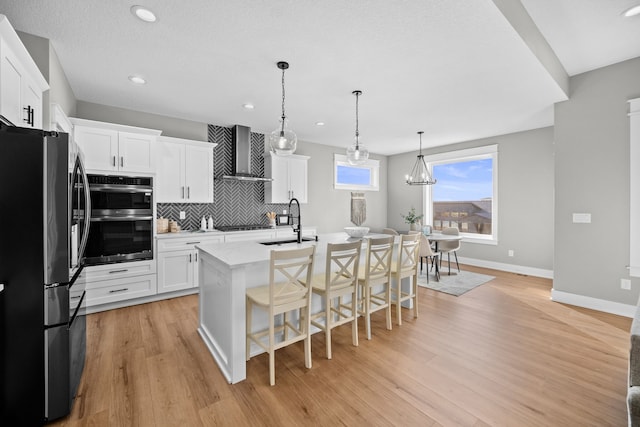 kitchen featuring a sink, stainless steel appliances, light wood-type flooring, wall chimney range hood, and backsplash