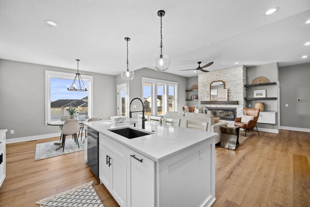 kitchen with a fireplace, hanging light fixtures, white cabinets, a sink, and light wood-type flooring