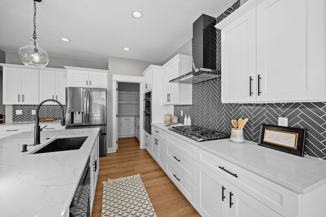 kitchen with stainless steel appliances, light wood-style flooring, white cabinetry, a sink, and wall chimney exhaust hood