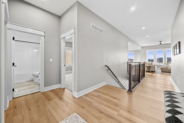 corridor with baseboards, visible vents, an upstairs landing, light wood-type flooring, and recessed lighting