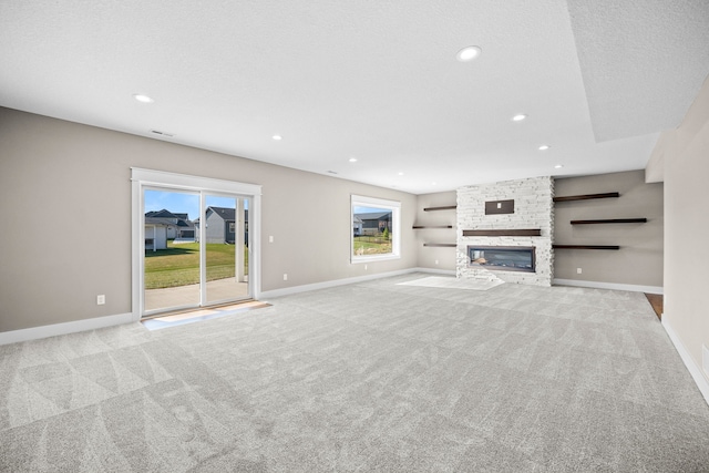 unfurnished living room featuring a stone fireplace, light colored carpet, and a textured ceiling