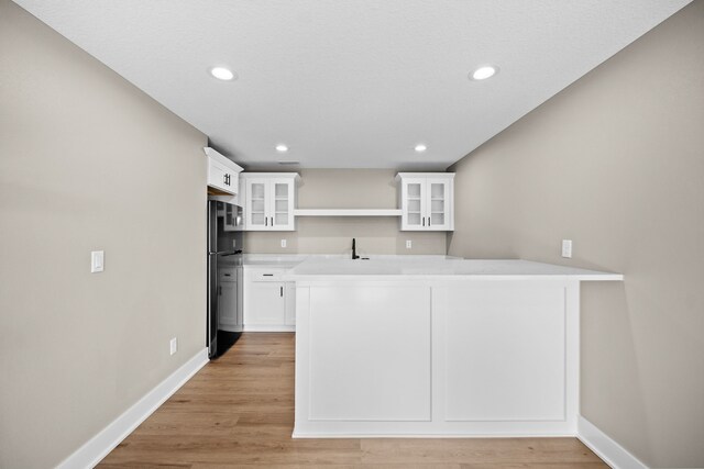 kitchen with open shelves, light wood finished floors, freestanding refrigerator, and white cabinetry