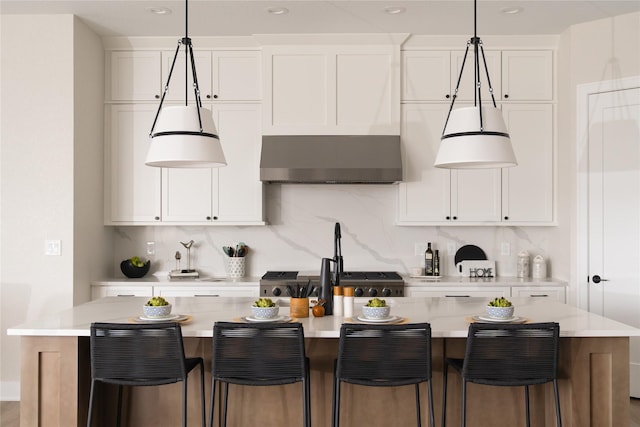 kitchen featuring decorative light fixtures, white cabinets, a kitchen breakfast bar, decorative backsplash, and a kitchen island with sink