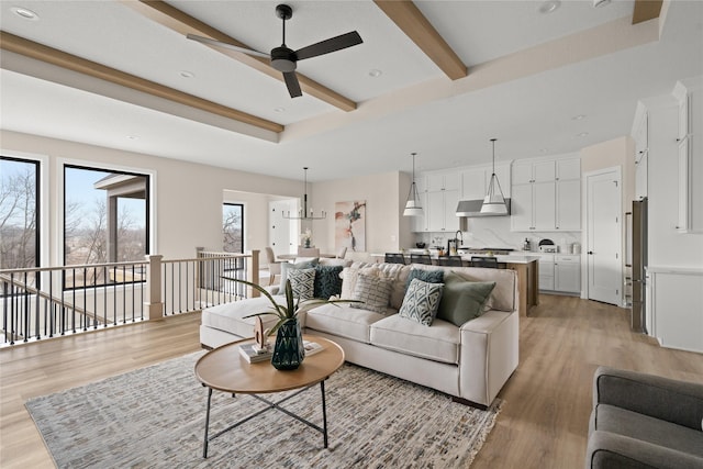 living room featuring beam ceiling, ceiling fan with notable chandelier, light wood-type flooring, and a tray ceiling