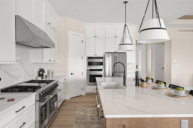 kitchen featuring hanging light fixtures, a center island with sink, premium appliances, light stone countertops, and exhaust hood