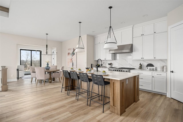 kitchen with white cabinetry, wall chimney range hood, hanging light fixtures, and an island with sink