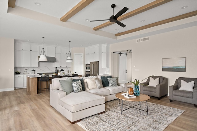 living room with beamed ceiling, a barn door, ceiling fan, and light wood-type flooring