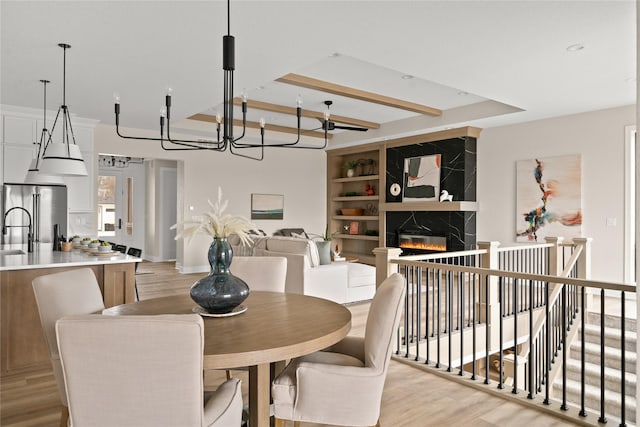 dining space with sink, a premium fireplace, a raised ceiling, and light hardwood / wood-style floors