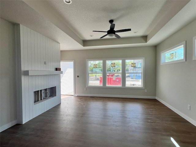 unfurnished living room with a ceiling fan, a textured ceiling, baseboards, dark wood-style flooring, and a raised ceiling