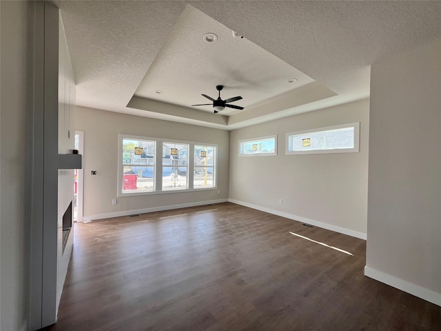unfurnished living room with a ceiling fan, a raised ceiling, baseboards, and a textured ceiling