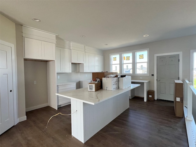 kitchen with a center island, light stone counters, white cabinetry, white microwave, and dark wood-style floors