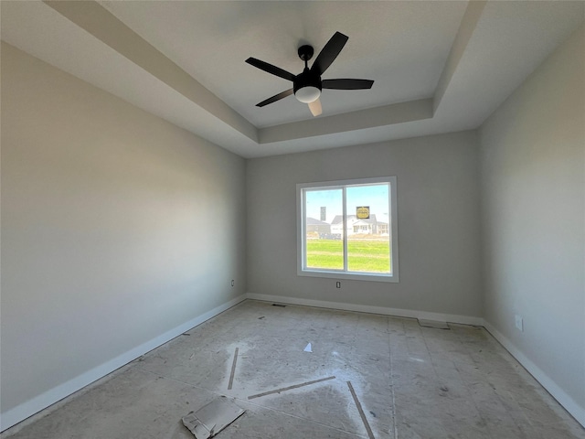 empty room with a tray ceiling, baseboards, and a ceiling fan