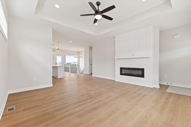 625 NW Georgetown Dr, Waukee, IA 50263 - unfurnished living room with a tray ceiling, light wood-style flooring, ceiling fan, a chandelier, and recessed lighting