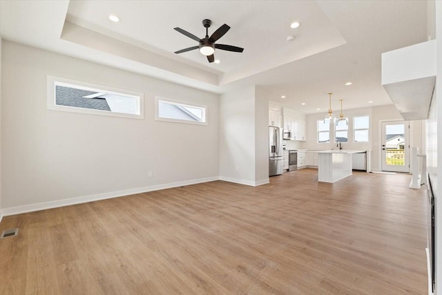 625 NW Georgetown Dr, Waukee, IA 50263 - unfurnished living room with a tray ceiling, light wood-style floors, healthy amount of natural light, recessed lighting, and a ceiling fan