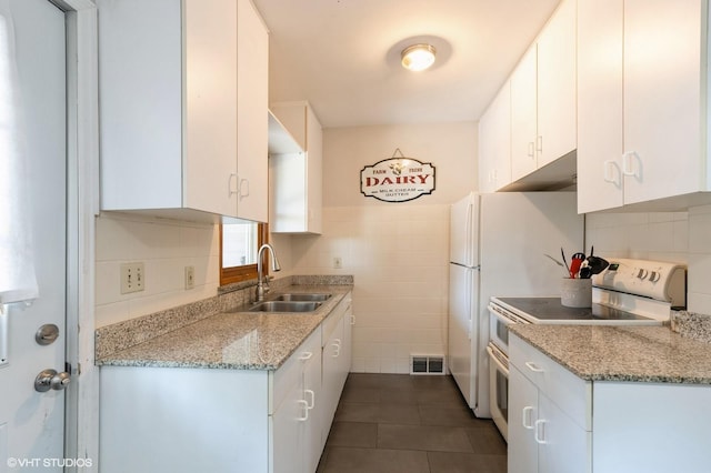 kitchen with white electric range, dark tile patterned flooring, sink, and white cabinets