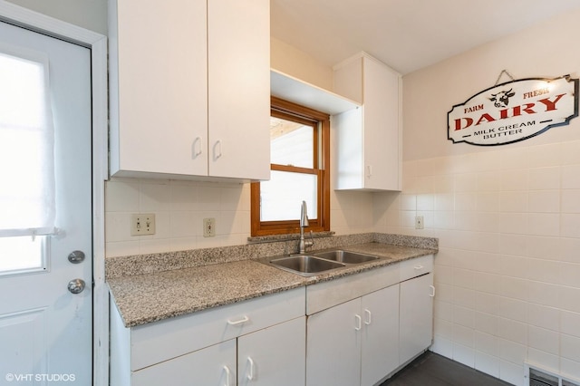 kitchen featuring white cabinetry, sink, light stone counters, and tile walls