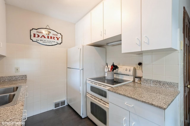 kitchen featuring tile walls, dark tile patterned flooring, white appliances, light stone countertops, and white cabinets