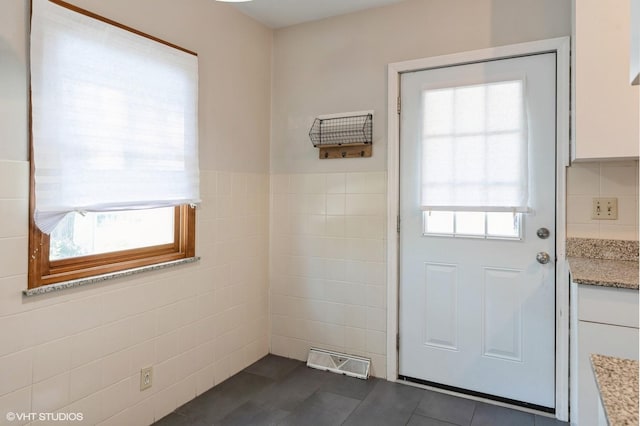 doorway with dark tile patterned floors and tile walls