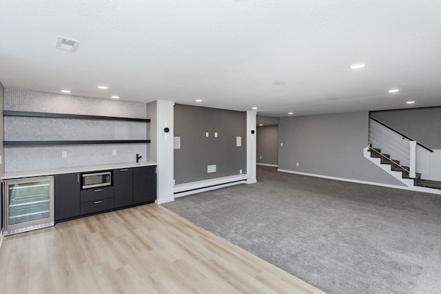 unfurnished living room featuring a baseboard radiator, indoor bar, wine cooler, and light hardwood / wood-style floors