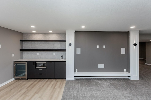 bar with stainless steel microwave, beverage cooler, and light hardwood / wood-style floors