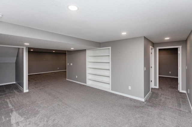 basement featuring dark carpet, built in features, and a textured ceiling