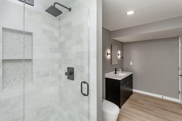 bathroom featuring hardwood / wood-style flooring, vanity, toilet, a shower with door, and a textured ceiling