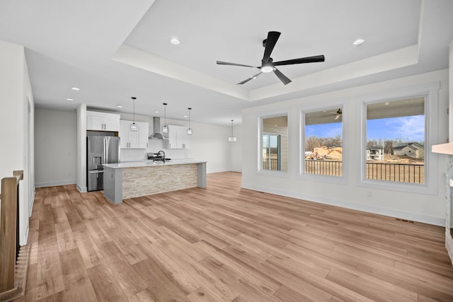 unfurnished living room with a raised ceiling, sink, ceiling fan, and light hardwood / wood-style flooring