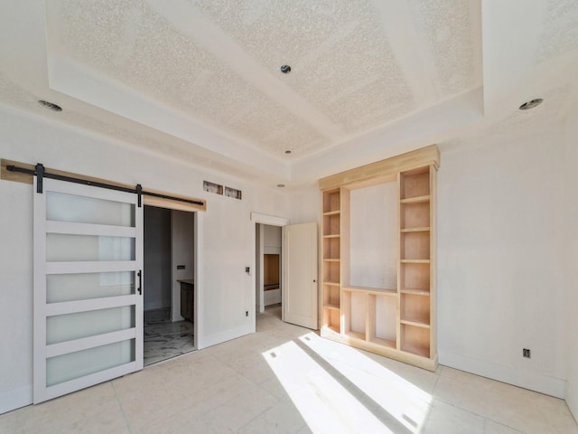 unfurnished bedroom with a tray ceiling, a barn door, and a textured ceiling