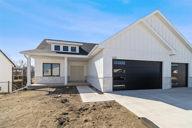 modern farmhouse featuring board and batten siding, a shingled roof, a garage, stone siding, and driveway