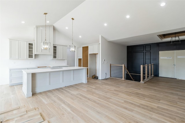 kitchen with light wood-style flooring, a spacious island, white cabinets, light countertops, and glass insert cabinets