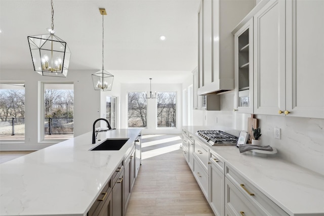 kitchen with a wealth of natural light, light wood-type flooring, a notable chandelier, and a sink