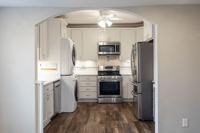 kitchen with appliances with stainless steel finishes, white cabinets, stacked washer and clothes dryer, ceiling fan, and dark wood-type flooring