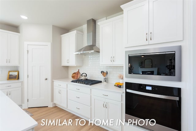 kitchen featuring wall chimney exhaust hood, wall oven, built in microwave, stainless steel gas cooktop, and white cabinets