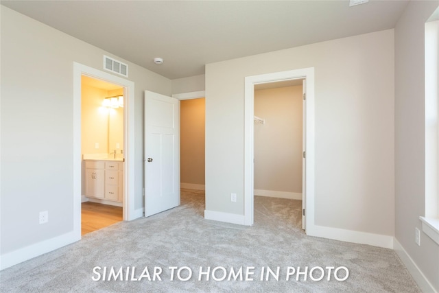 unfurnished bedroom with carpet floors, a spacious closet, baseboards, and ensuite bath