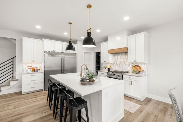 kitchen with pendant lighting, white cabinets, a kitchen island with sink, and premium appliances