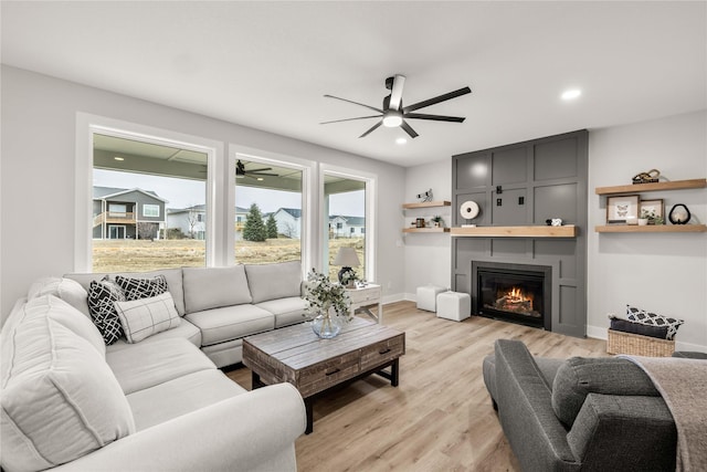 living room with a large fireplace, ceiling fan, and light wood-type flooring