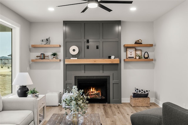 living room featuring a fireplace, light hardwood / wood-style flooring, and ceiling fan