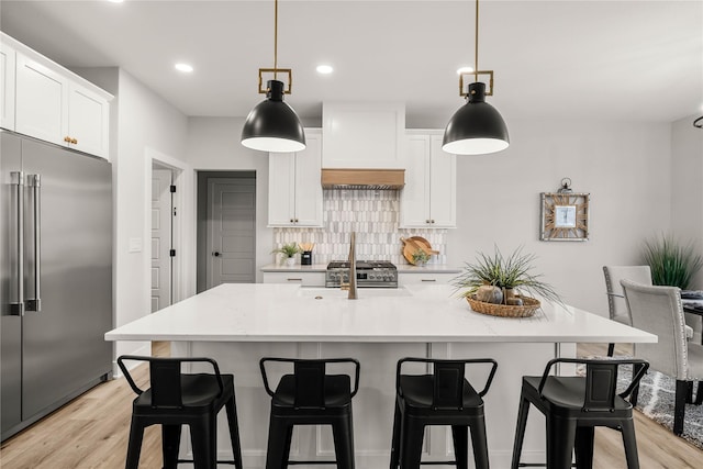 kitchen featuring white cabinetry, hanging light fixtures, a kitchen island with sink, and built in fridge