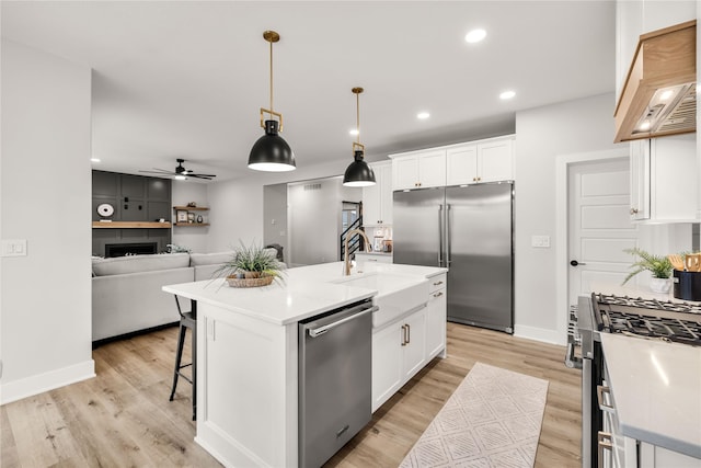 kitchen with custom exhaust hood, hanging light fixtures, a center island with sink, appliances with stainless steel finishes, and white cabinets