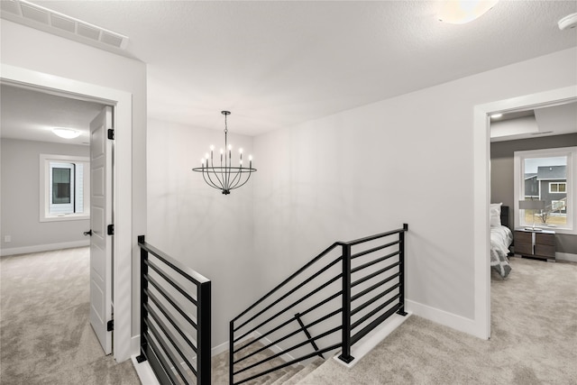 stairs with a notable chandelier, a textured ceiling, and carpet