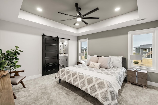 bedroom featuring a tray ceiling, a barn door, and light carpet