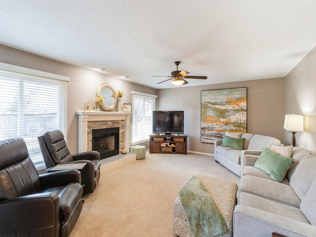 carpeted living room featuring ceiling fan, a stone fireplace, and a textured ceiling