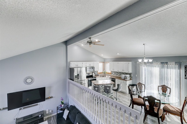 interior space with vaulted ceiling with beams, ceiling fan with notable chandelier, a textured ceiling, and light hardwood / wood-style floors