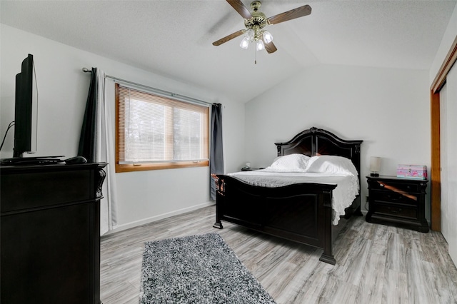 bedroom featuring ceiling fan, light hardwood / wood-style floors, vaulted ceiling, and a textured ceiling