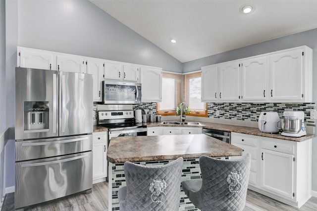 kitchen with lofted ceiling, sink, appliances with stainless steel finishes, white cabinetry, and a kitchen island